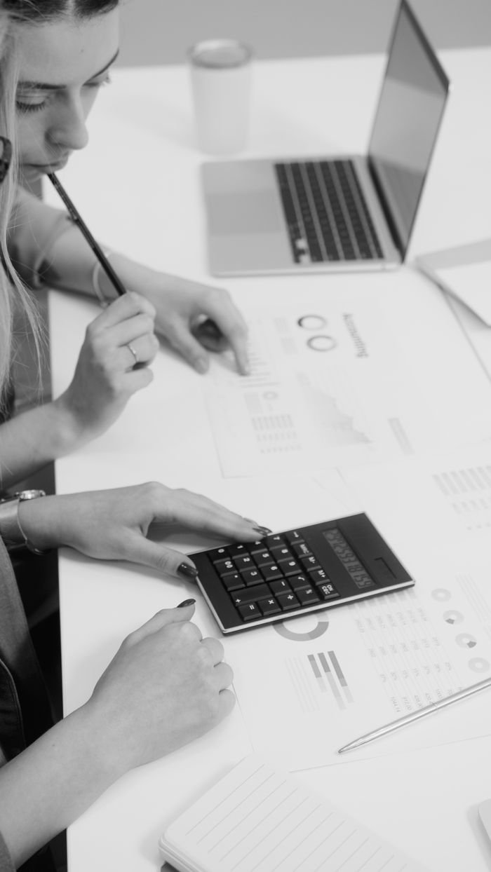 Home Two colleagues reviewing financial reports with a calculator in a modern workspace.